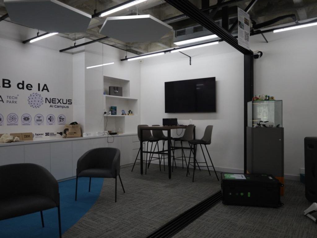 LAB de IA do Ágora Tech Park com mesas altas, poltronas e TV na parede